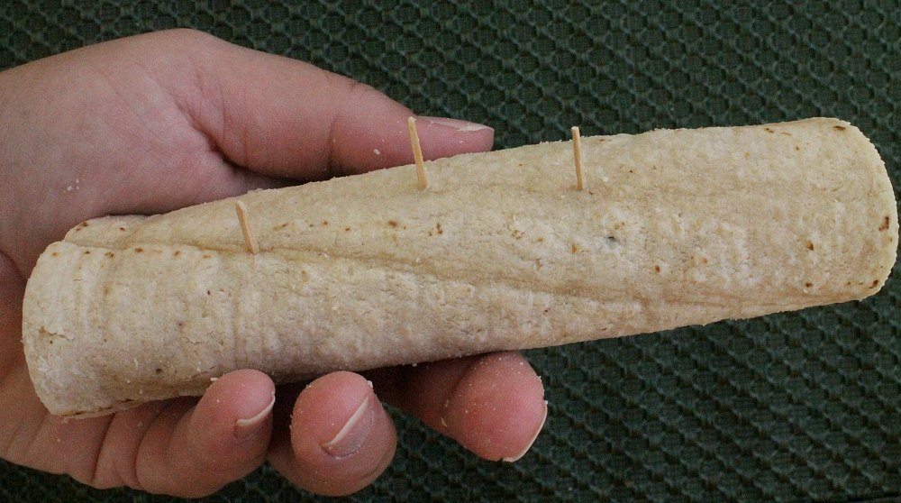 Hand holding a rolled up corn tortilla with toothpicks in the center