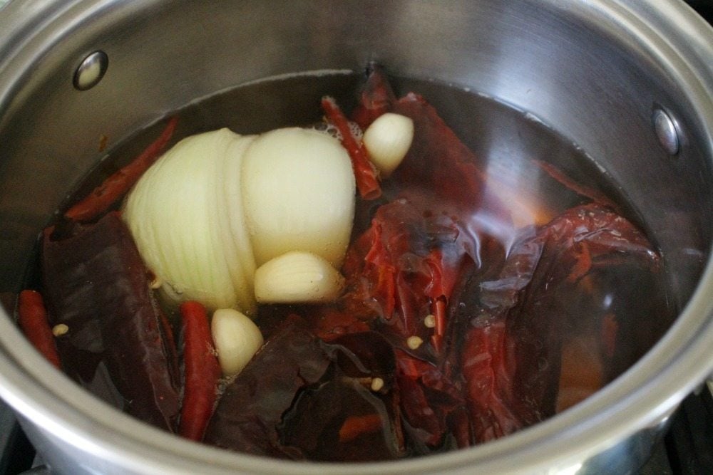 Chiles, onion, and garlic in a pot full of water.