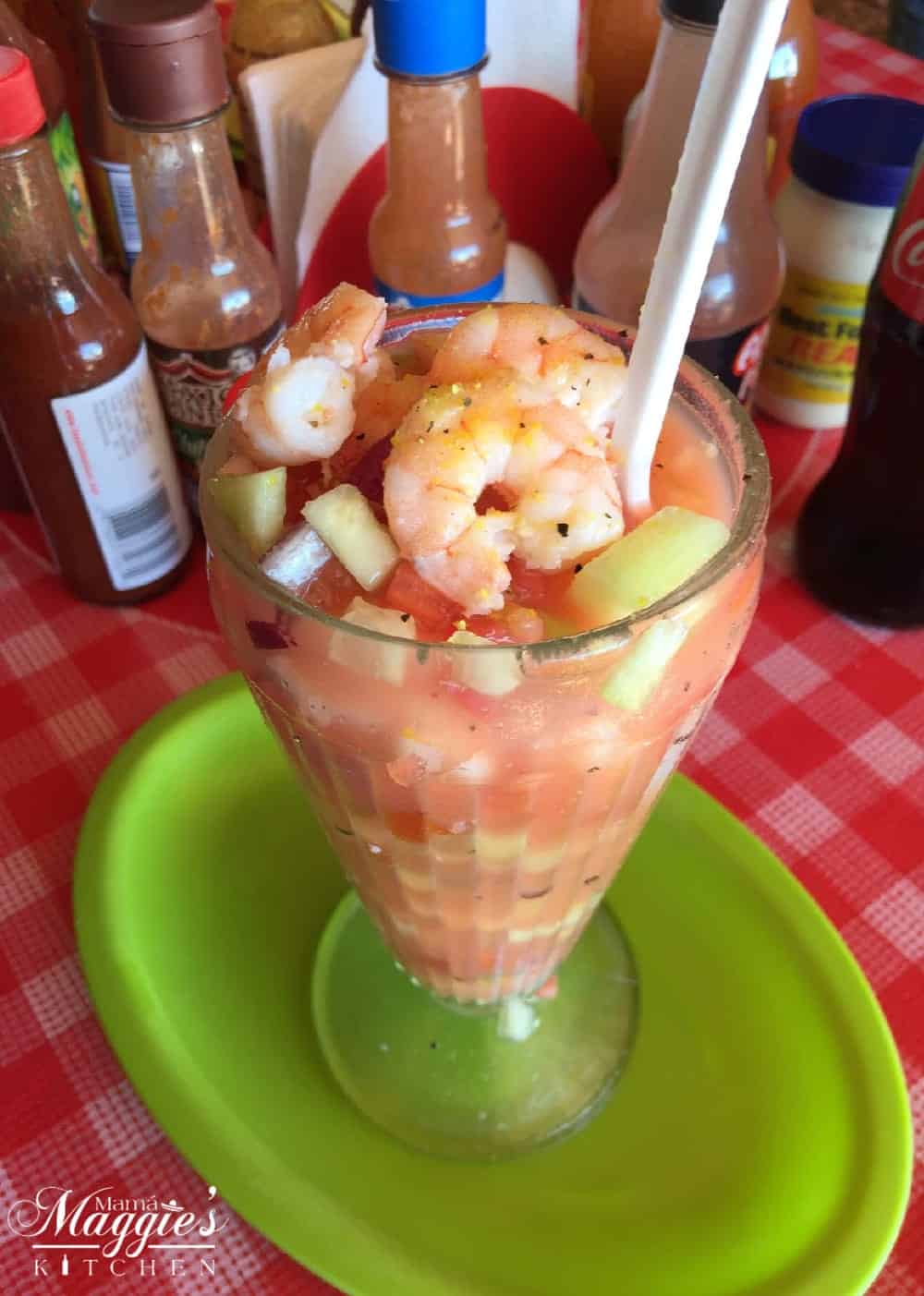 Coctel de Camarones (Mexican Shrimp Cocktail) in a glass on a green plate and red checkered tablecloth.