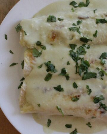 Enchiladas Suizas on a white plate topped with chopped cilantro