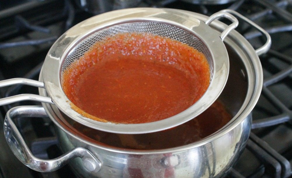 A spicy tomato sauce straining through a strainer over a pot.