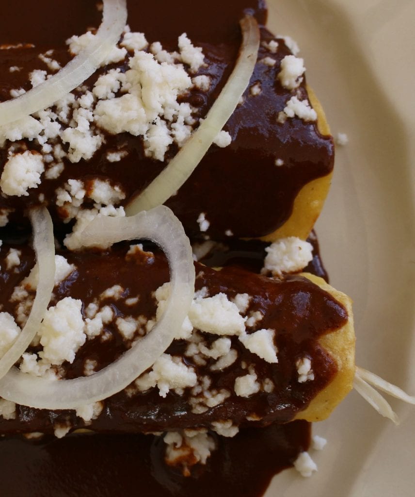 Chicken Mole Enchiladas topped with queso fresco and slices of onion.