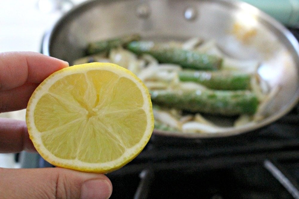A hand holding half a lemon with a skillet in the background.
