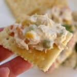 Hand holding saltine cracker topped with Mexican Chicken Salad, or Ensalada de Pollo