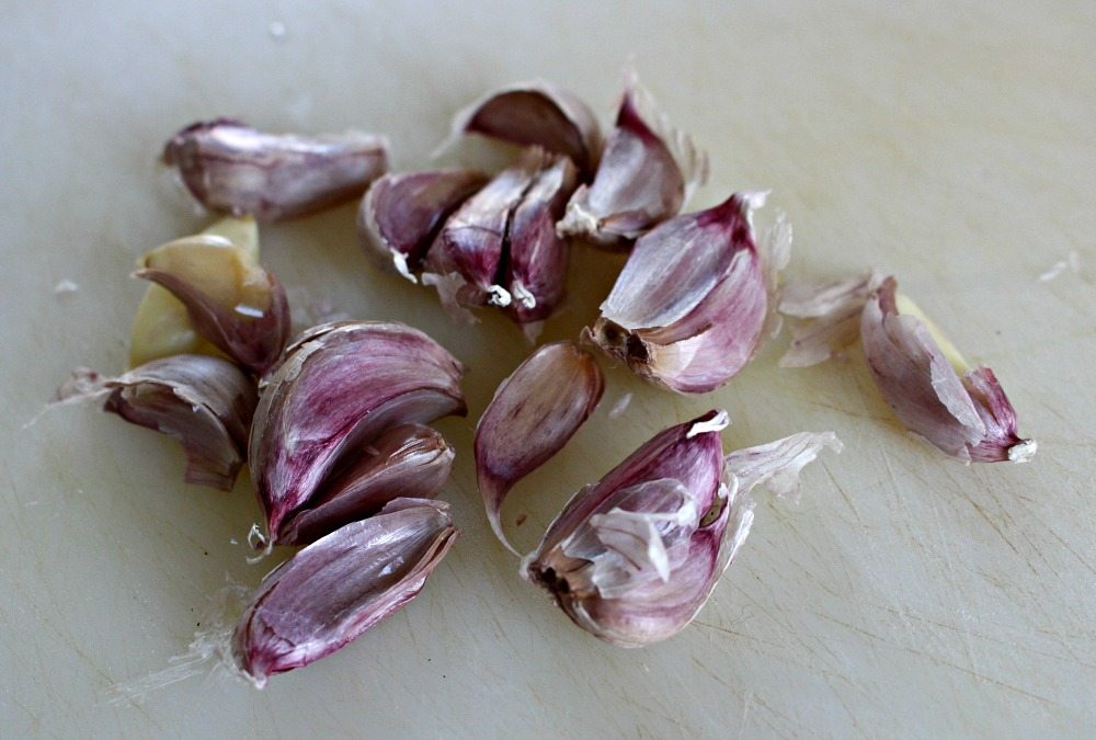 Raw Unpeeled Garlic on a white cutting board.