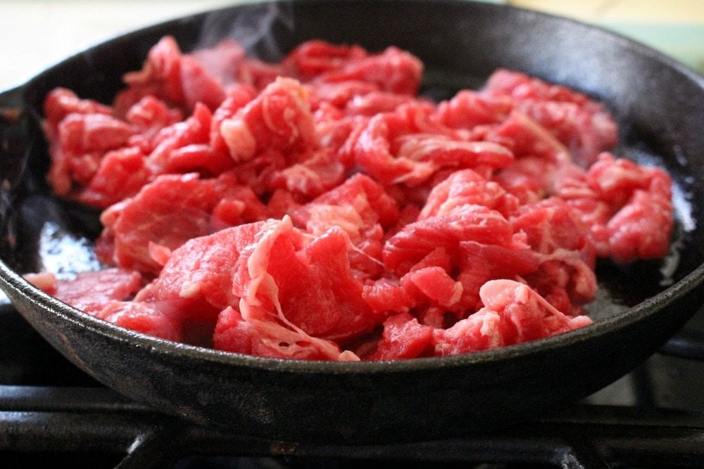 Raw red meat cooking in black cast iron skillet