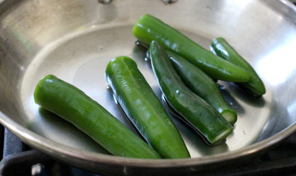 Whole serrano peppers cooking in a skillet.