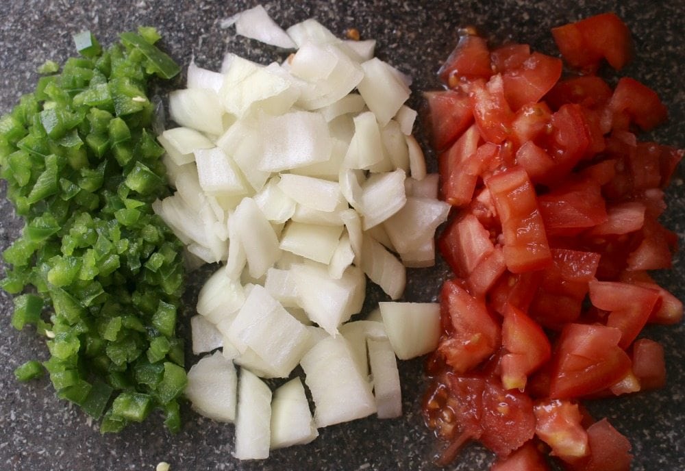 Diced Jalapenos, onions, and tomatoes on a cutting board.