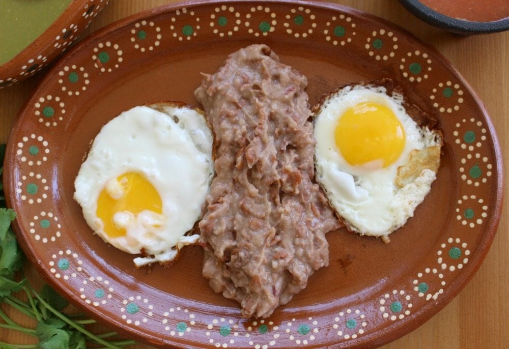 Two sunny-side up eggs separated by refried beans and served on a decorative Mexican plate.