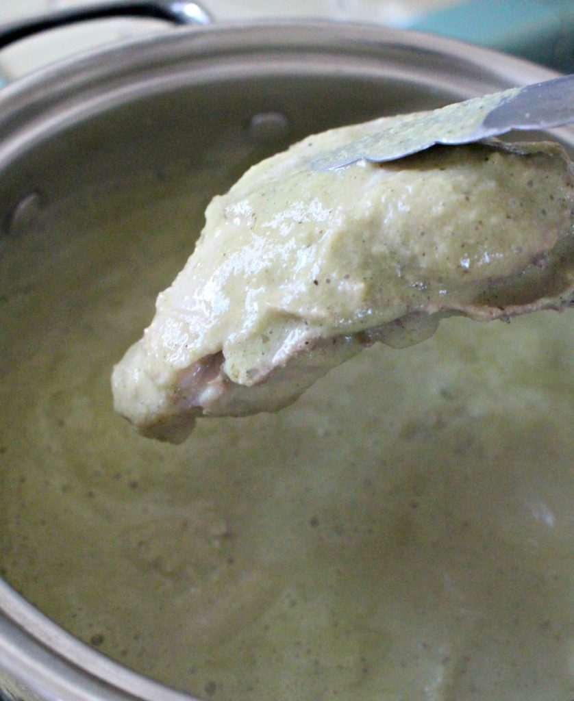 Tongs placing chicken in Pipián Verde sauce