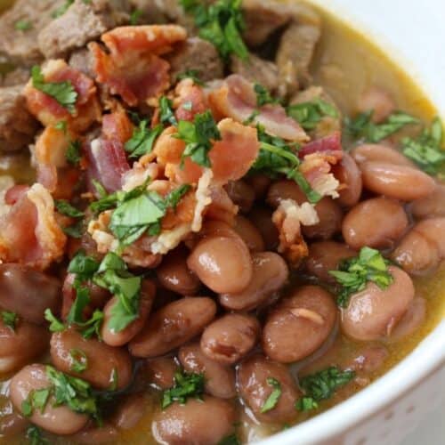 Carne En Su Jugo in a white bowl topped with cilantro beans bacon