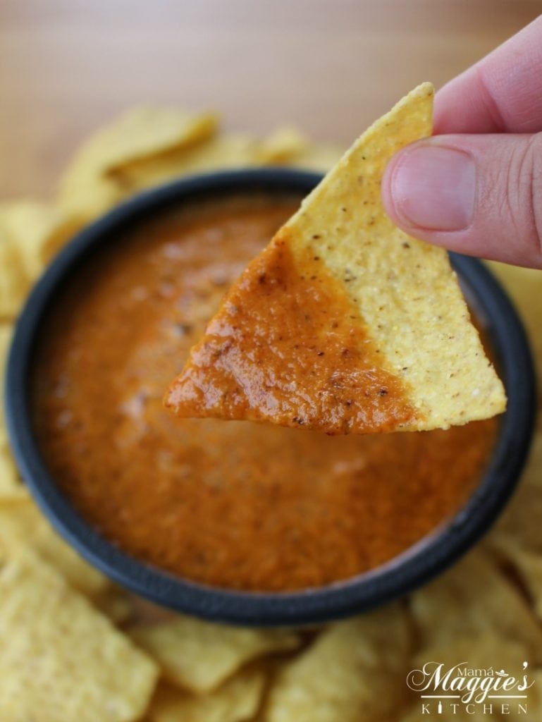 Hand holding a chip with Chile de Arbol Salsa.
