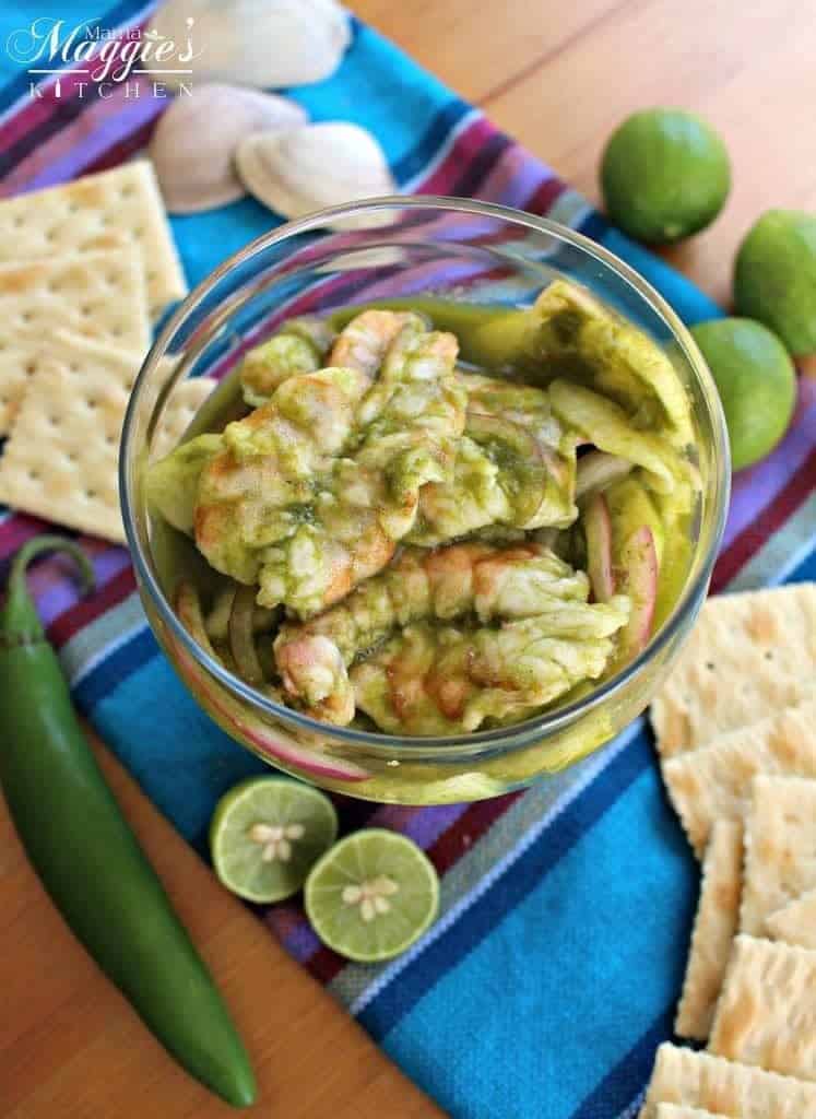 Aguachiles, or Shrimp in Spicy Green Chile Sauce, surrounded by crackers, lime and decorative Mexican tablecloth