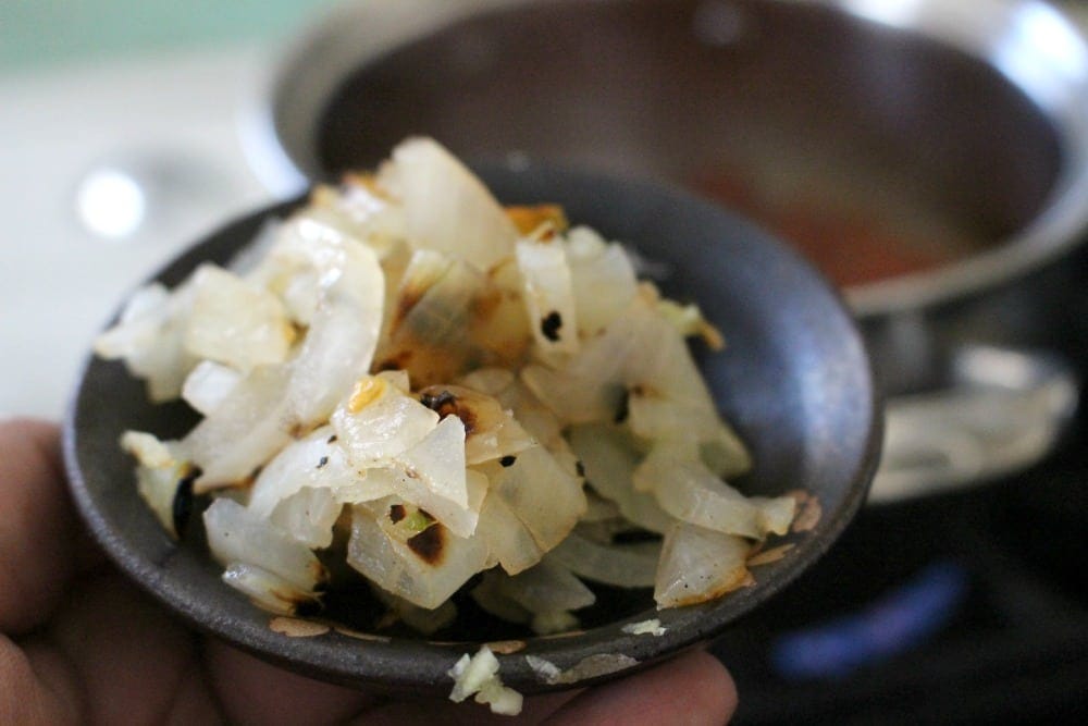 Hand holding small plate of chopped grilled onions over the stove