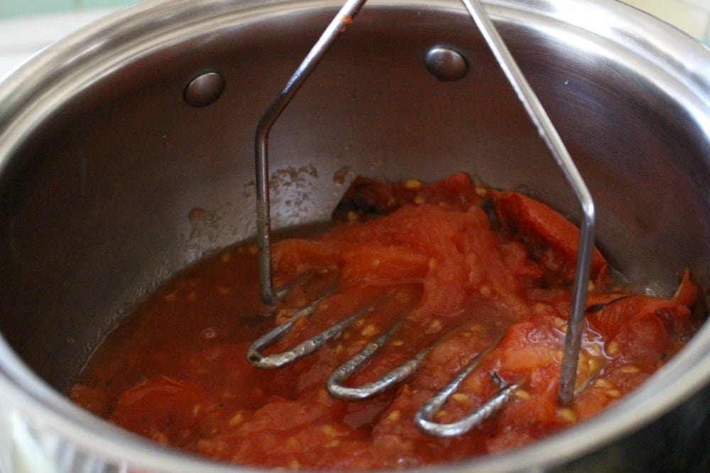 Potato masher mashing tomatoes in a stock pot