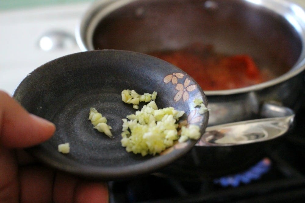 Hand holding small plate of minced garlic over the stove