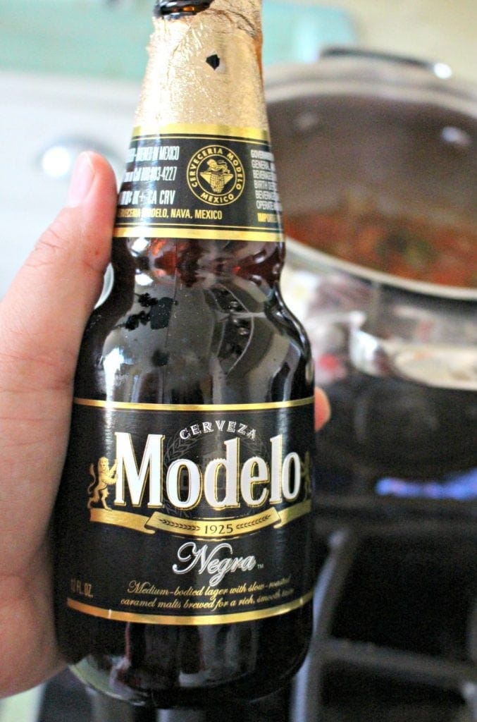 Hand holding bottle of Modelo Negro over the stove