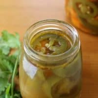 Pickled Jalapenos Chiles en Vinagre surrounded by jar and cilantro.