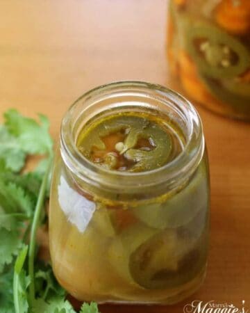 Pickled Jalapenos Chiles en Vinagre surrounded by jar and cilantro.