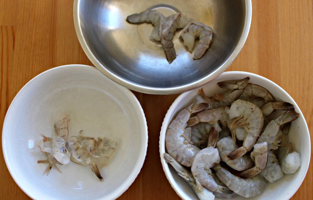 Three bowls with shrimp shells, another with peeled shrimp, and lastly a bowl of shrimp with shells on. 