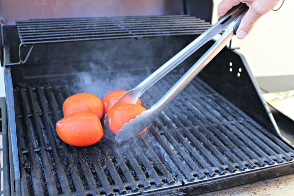 Tongs putting tomatoes on the grill