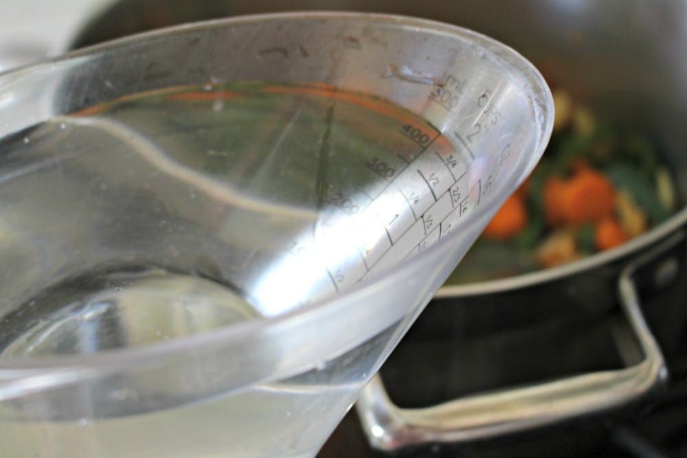 Measuring cup with white distilled vinegar over a stock pot.