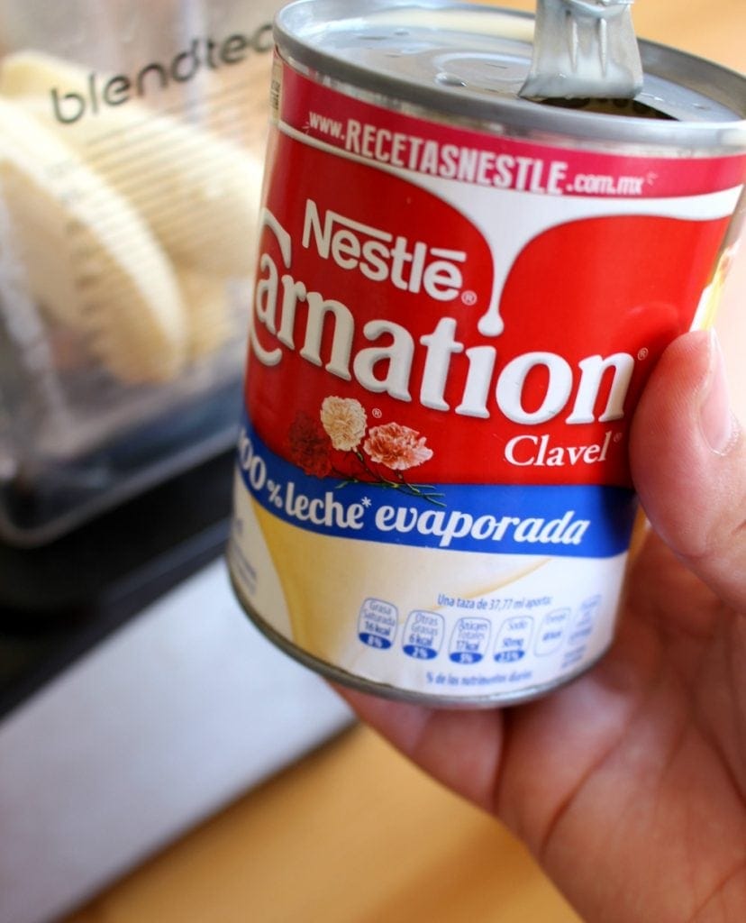 Hand holding can of Nestle Carnation Evaporated Milk next to blender