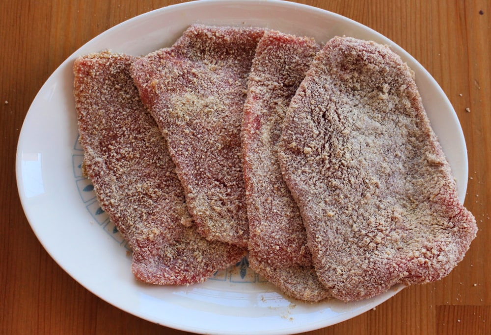 Four breaded milanesa steaks on a white plate. 