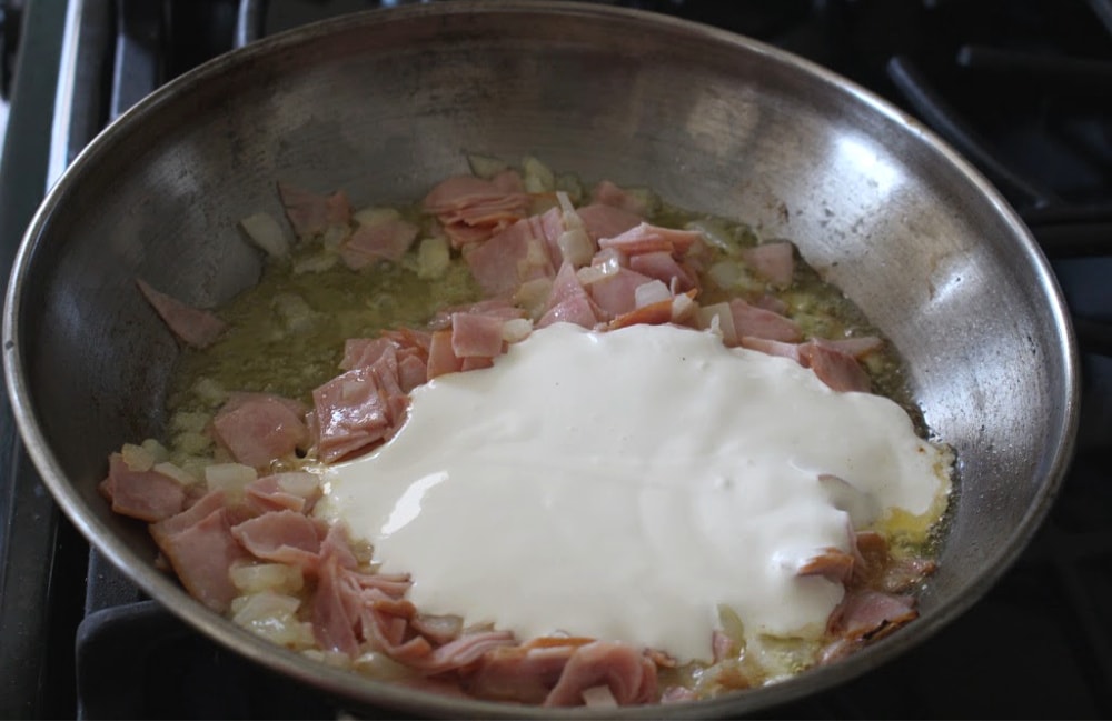 Crema mexicana in a skillet with diced ham and onions