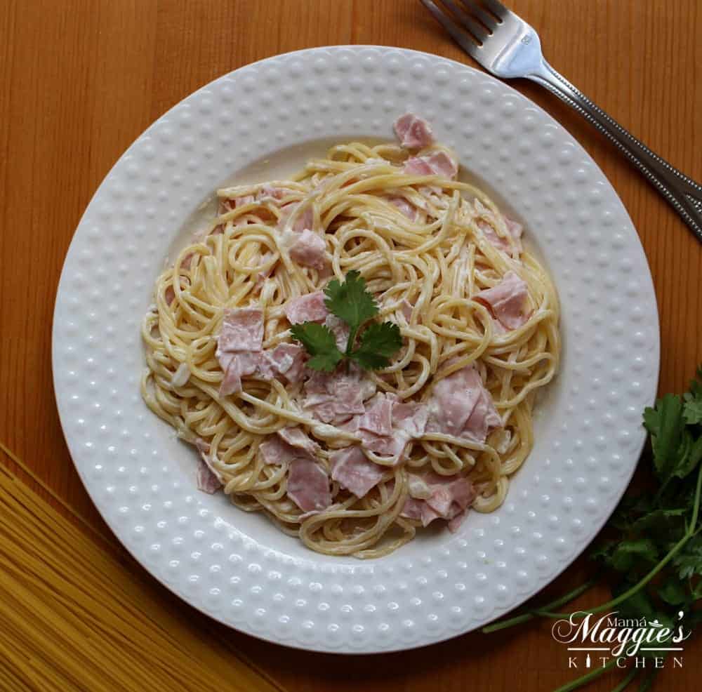 Espagueti a la Crema, Spaghetti with Ham and Cream Sauce, on white plate surrounded by dried pasta and a fork