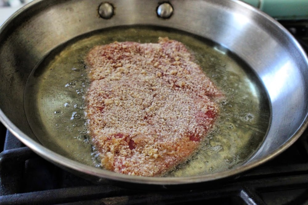 Breaded meat cooking in hot oil. Oil bubbles surround the meat in the skillet. 