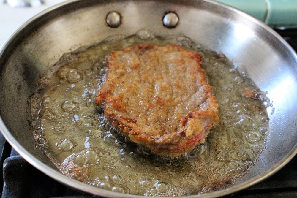 Meat cooking in hot, boiling oil in a metal skillet.