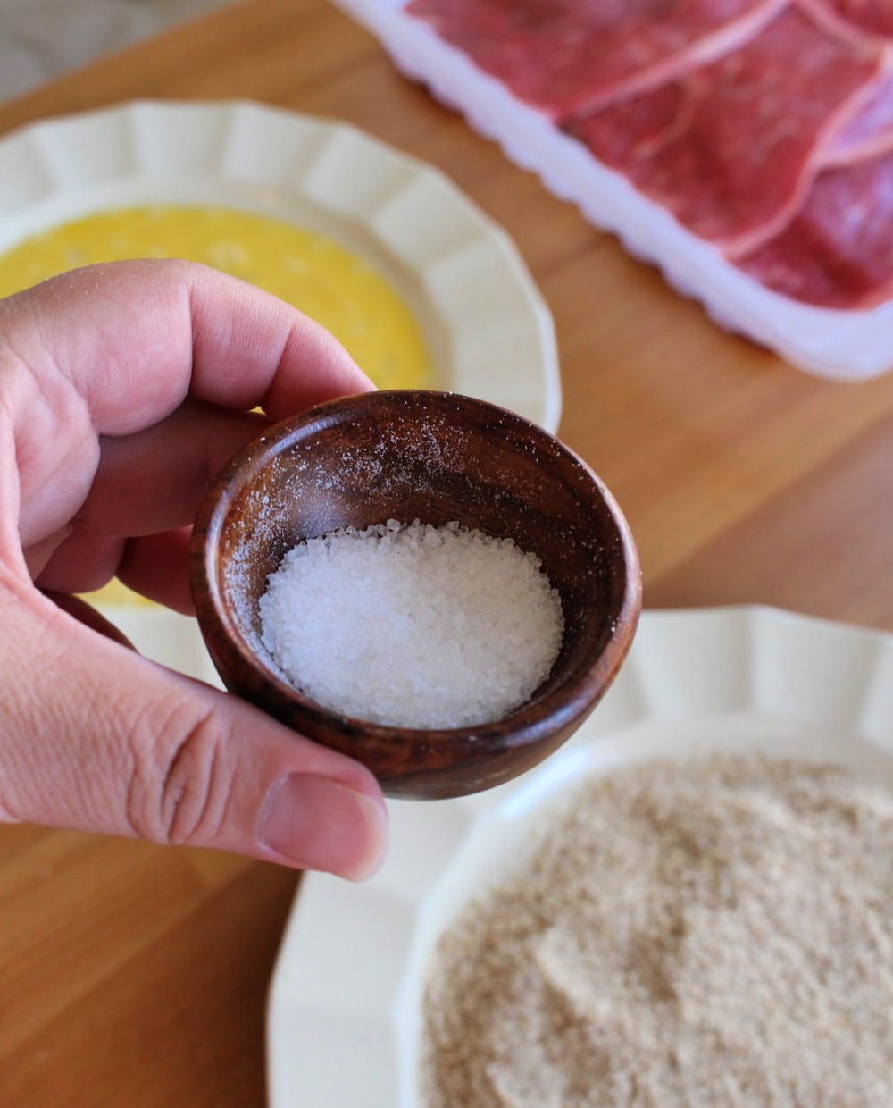 Hand holding a small brown plate filled with sea salt. 