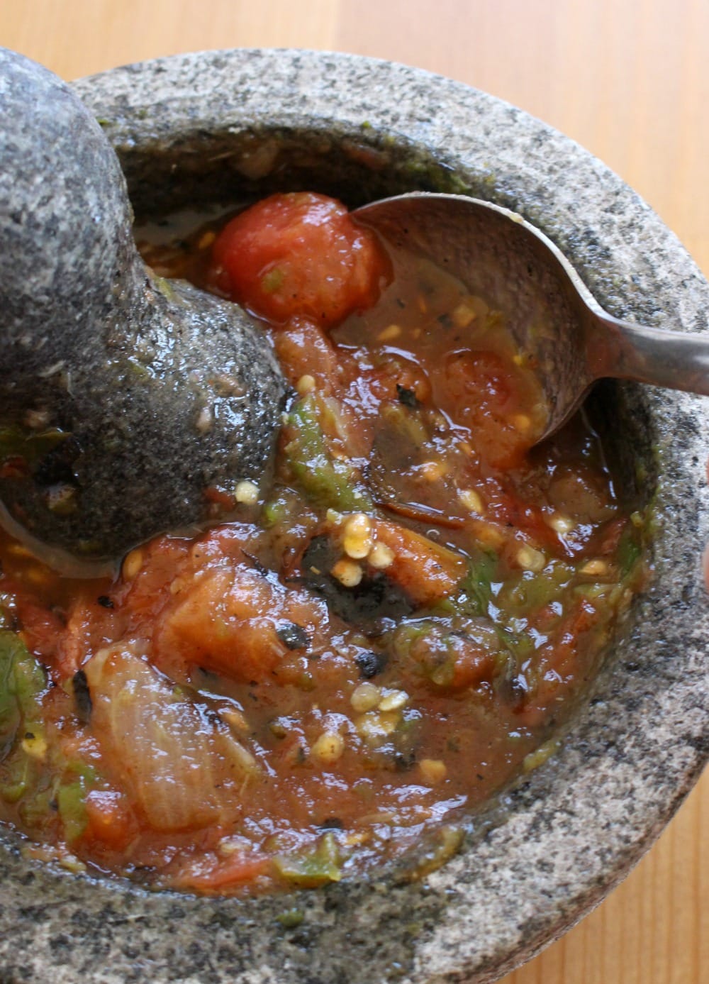 A spoon in a molcajete mixing the tomato salsa.