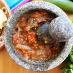 Tomato molcajete salsa surrounded by cilantro, jalapeno, and chips.