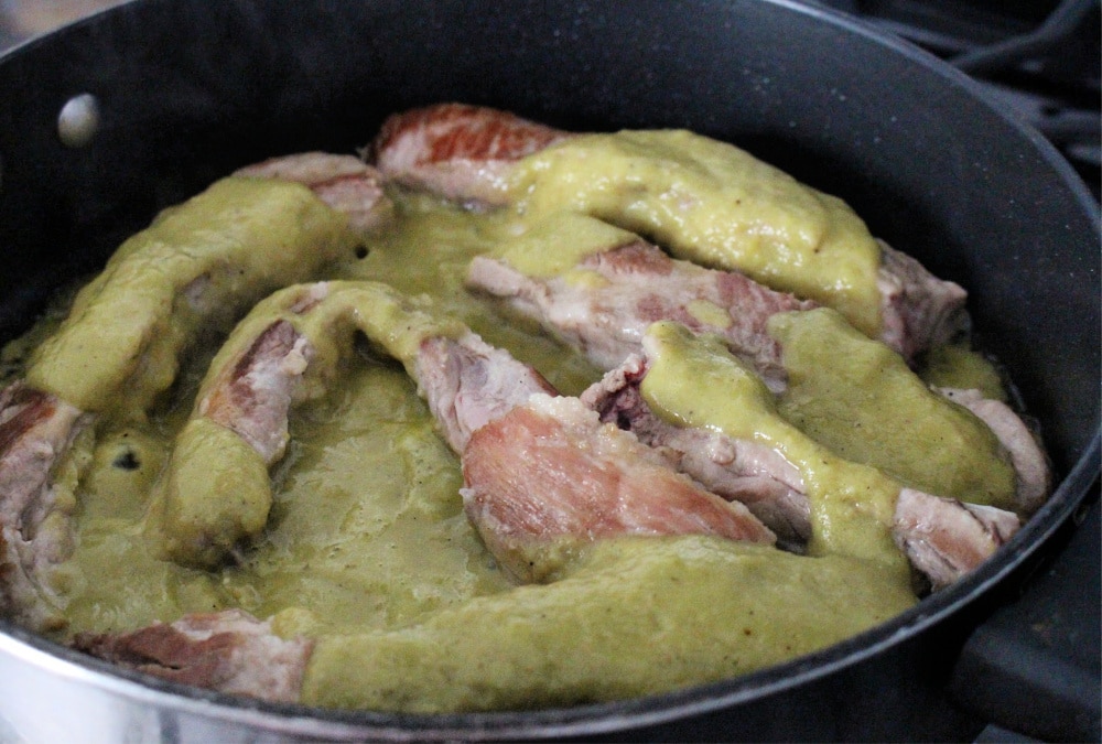 Green Salsa Verde cooking with pork ribs in a black skillet. 