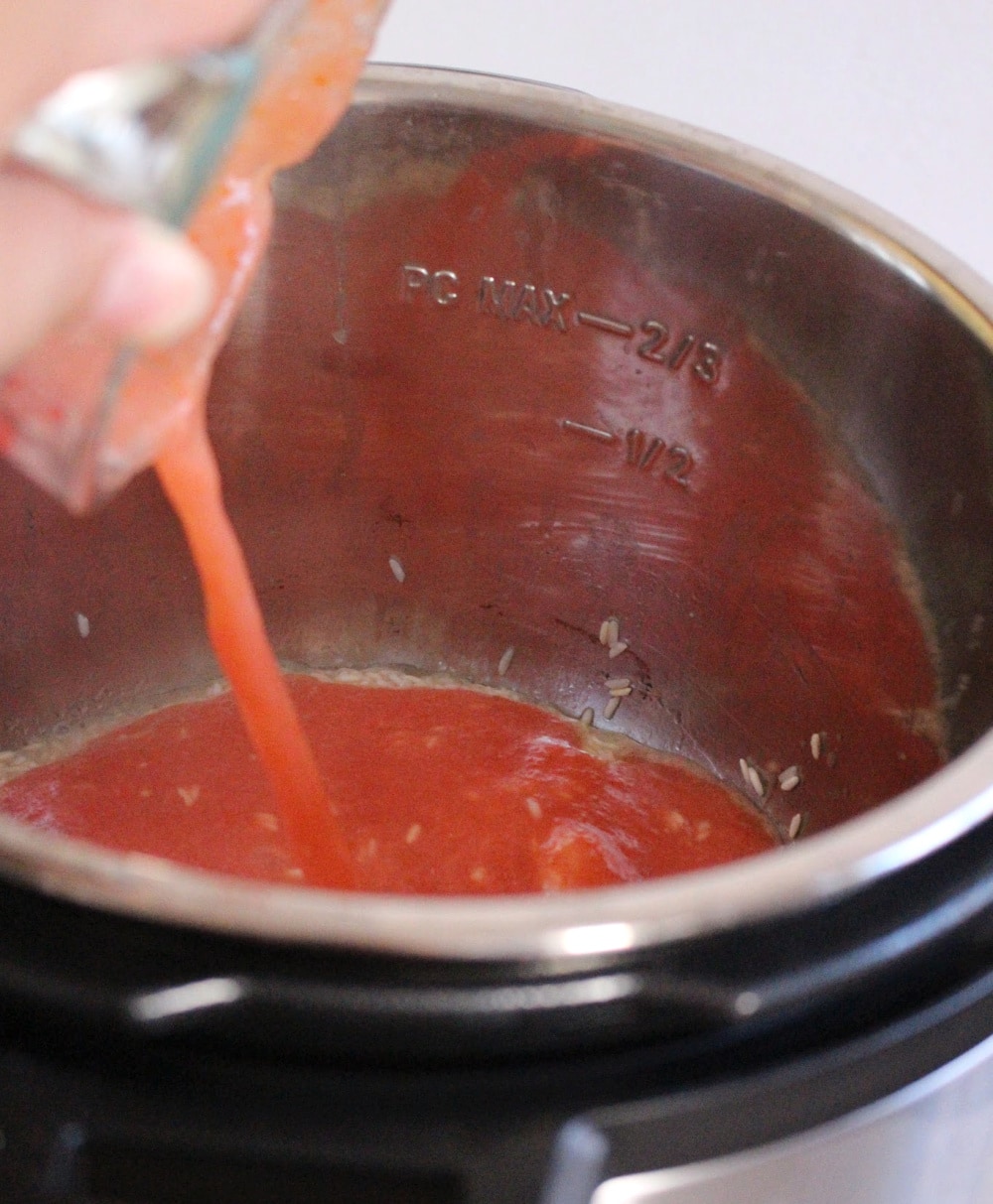 Cup pouring tomato sauce inside the instant pot. 