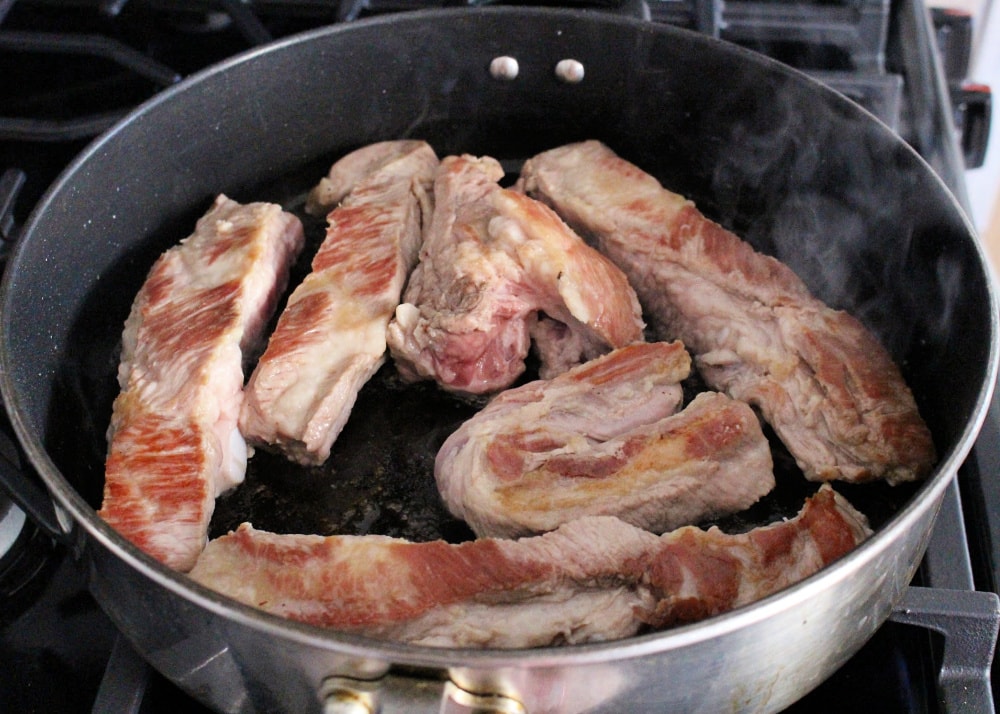 Browned ribs cooking in a black skillet. 
