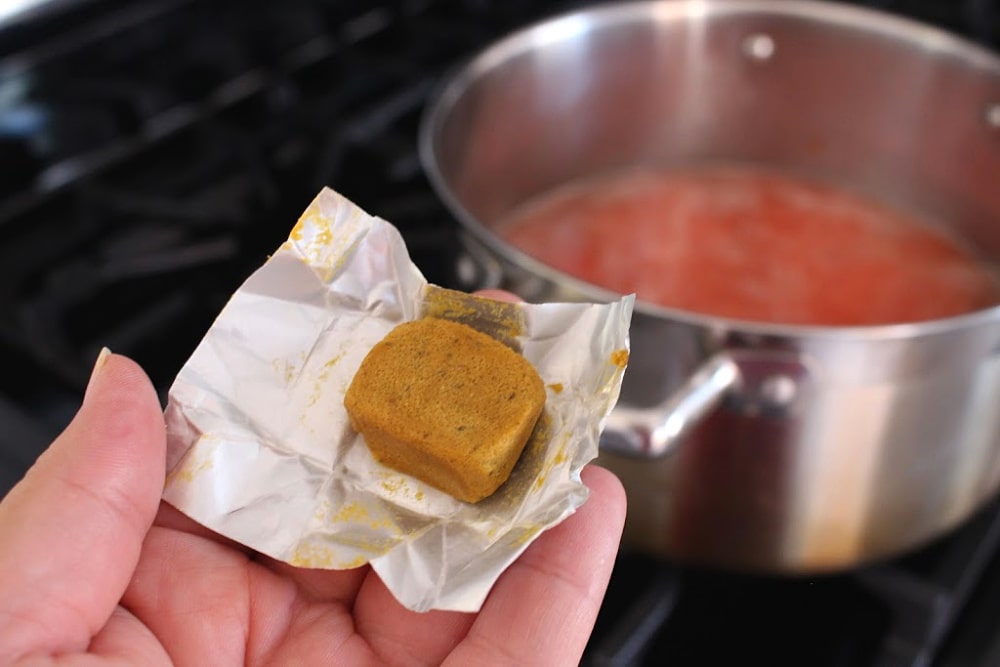 Hand holding a cube of chicken bouillon. 
