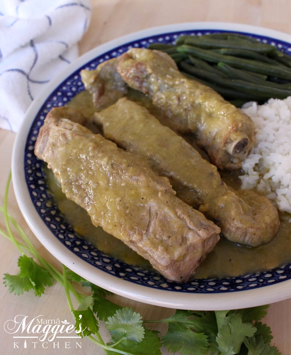 Costillas en Salsa Verde, or Ribs in Mexican Green Salsa, served on a blue plate with rice and green beans.