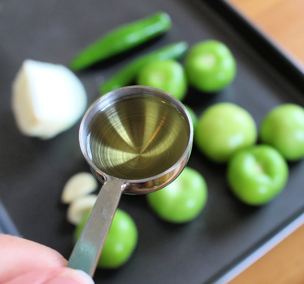 Hand holding a tablespoon of olive oil over a baking sheet. 