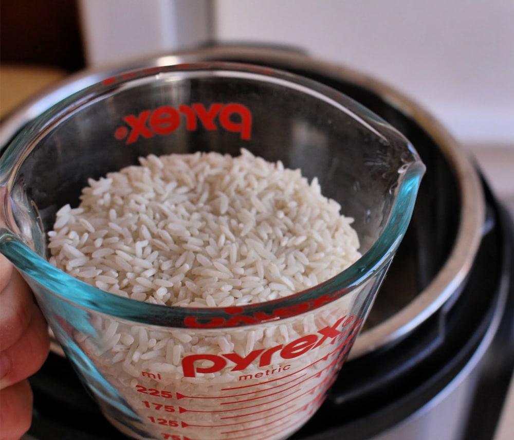 A measuring cup filled with rice over the instant pot. 