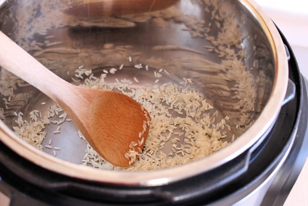 Wooden spoon stirring white rice in an instant pot. 