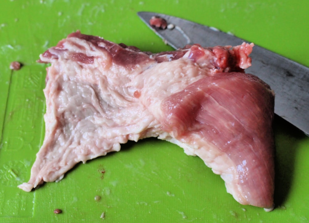 Knife cutting fat off ribs on a green cutting board. 