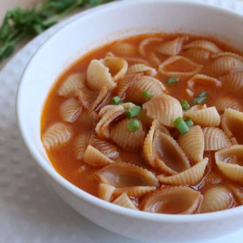 Sopa de Conchas, or Mexican Shell Pasta Soup, in a white bowl and topped with a few slices of green onions.