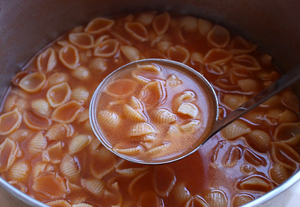 A ladle full of Sopa de Conchas over a stock pot of the soup. 