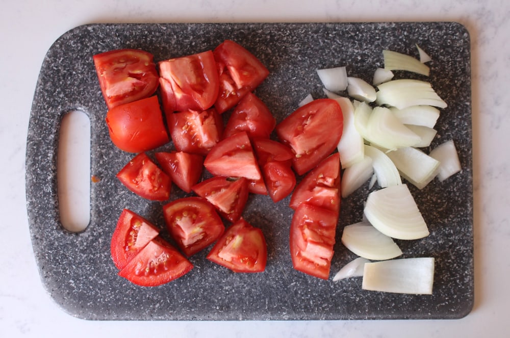 Chopped tomatoes and chopped onions on a cutting board.
