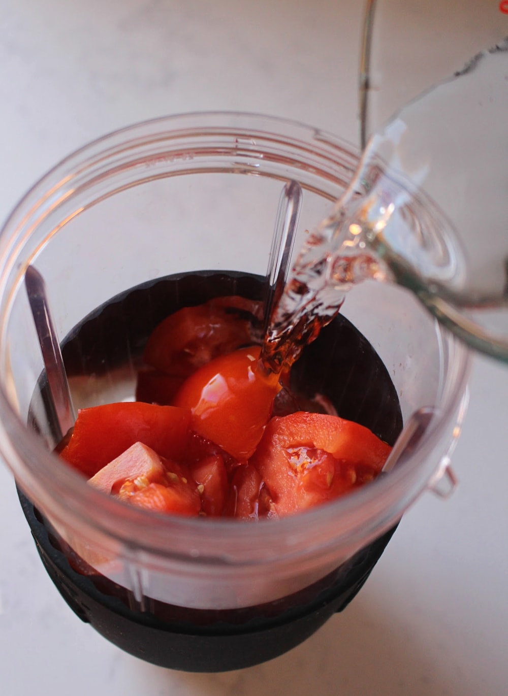 Water pouring into a blender filled with tomatoes. 