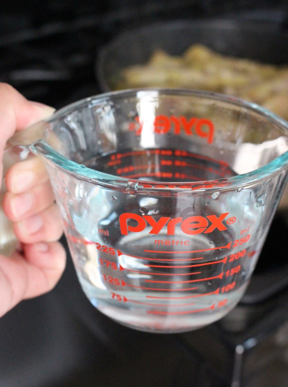 Hand holding a glass measuring cup with water. 