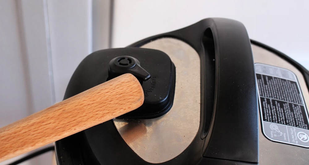 Back of a wooden spoon pushing the instant pot knob to venting. 